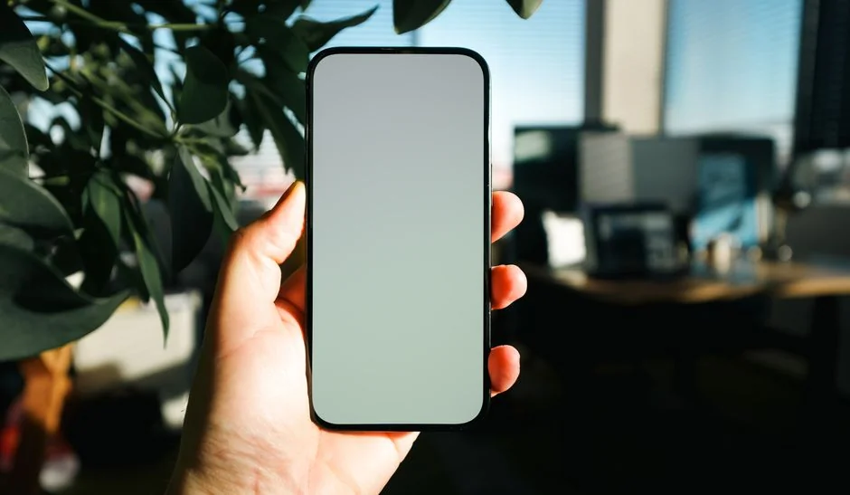 Close-up of a smartphone displaying a blurred image, placed on a desk beside a laptop.